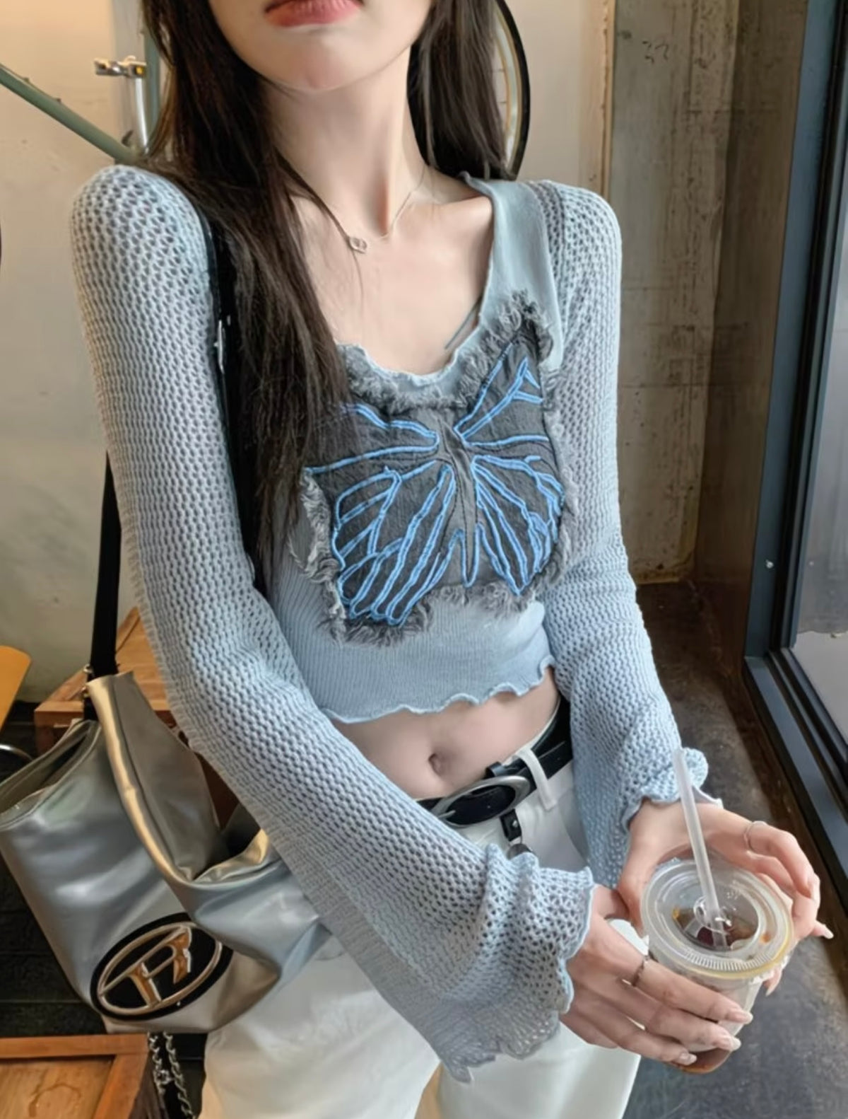 Close-up of butterfly appliqué and bell sleeves on light blue knit crop top